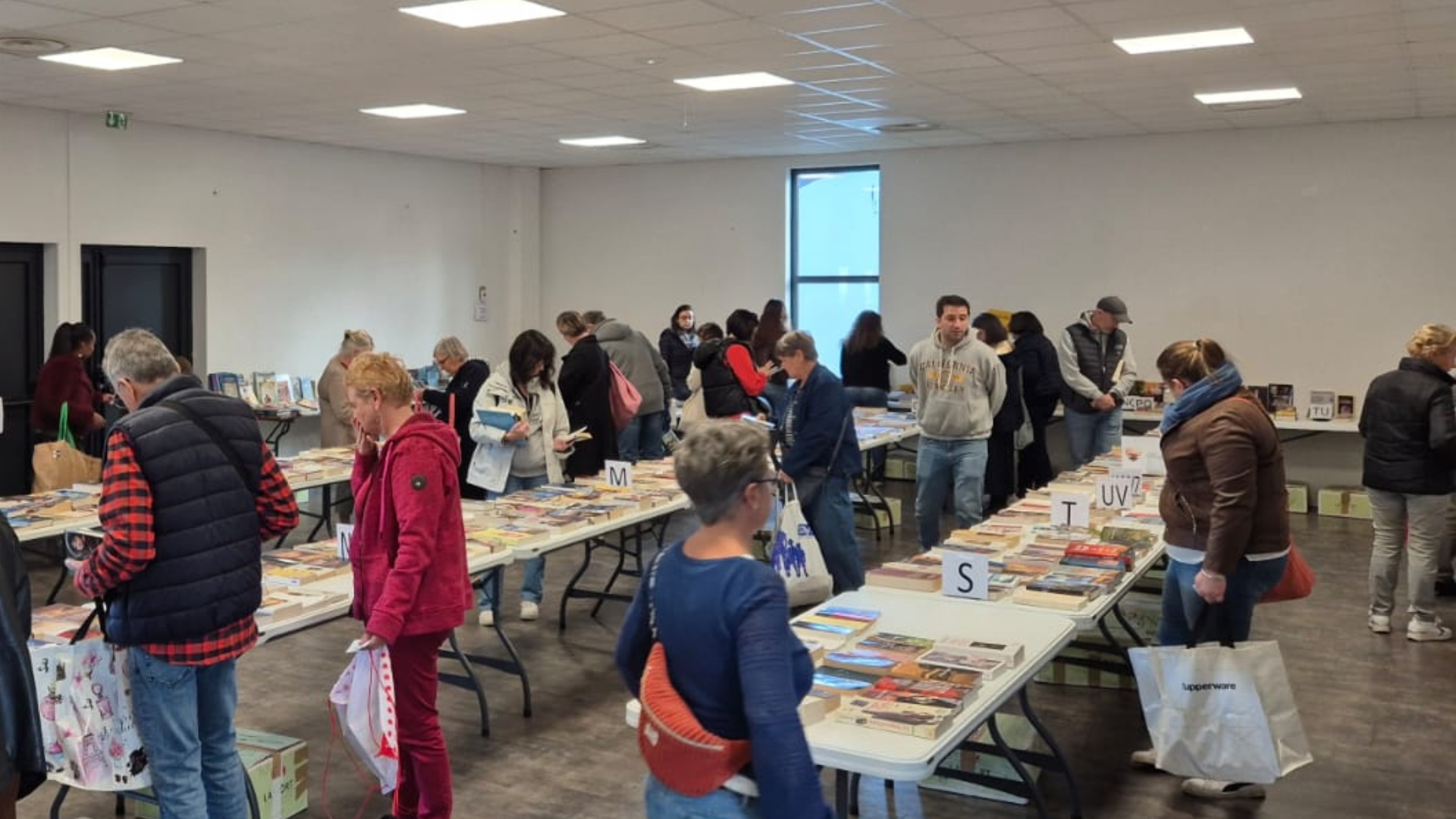 des personnes dans une salle en train de regarder des livres posés sur des rangées de tables