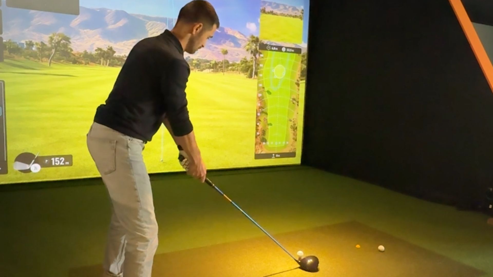 Un homme fait du golf dans une salle en intérieur devant un écran de practice