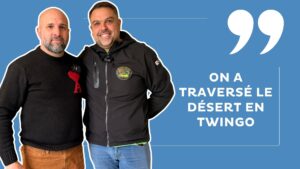 deux hommes en vestes noires posent devant un fond bleu. Texte : On a traversé le désert en Twingo