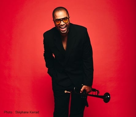 Un homme en noir tient une trompette. il pose sur fond rouge