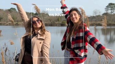 deux jeunes femmes lève les bras devan un "étang" entourée de fleur de pampa. L'une porte une veste beige l'autreun manteau à carreaux rouges et blancs