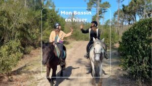 Deux jeunes femmes l'une en veste beige et l'autre noir sont sur des chevaux marron et blanc dans un chemin sableux en forêt