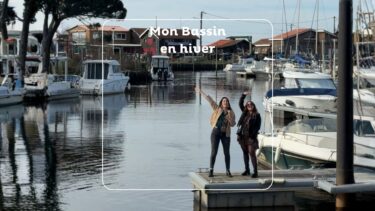 deux jeunes femmes sur le ponton d'un port. au loin des cbanes en bois.