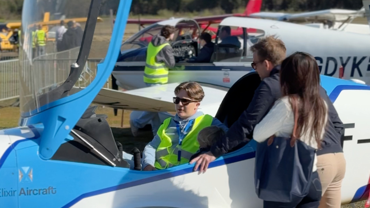 Un jeune homme avec un gilet jaune dans le cockpit d'un petit avion. il parle à deux autres personnes au milieu d'autres avions