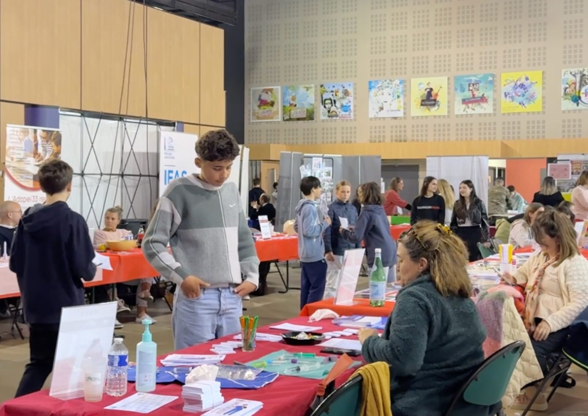 Des collégiens échangent avec des professionnels sur différents stands lors du forum PassNord dans une salle avec des tables et de la documentation