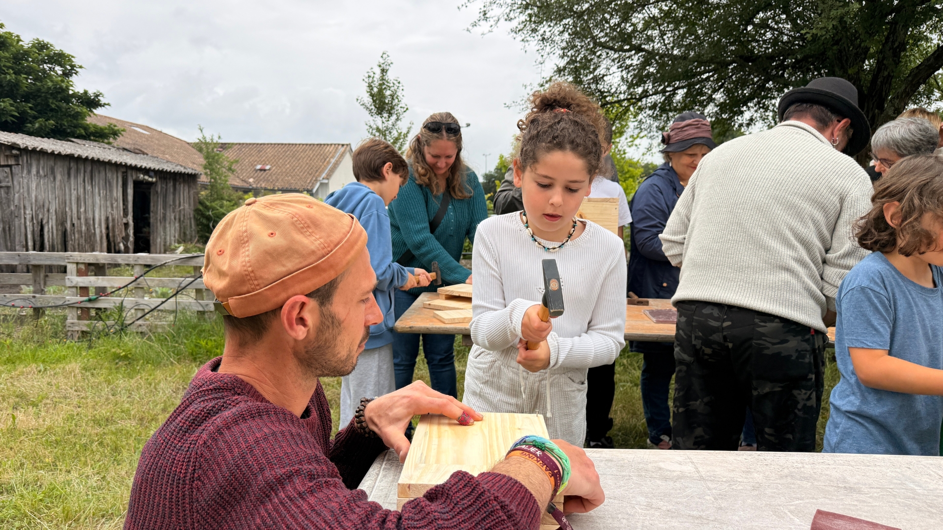 jeune enfant qui tient un marteau face à une table avec une planche en bois, un homme accroupi à côté de la table