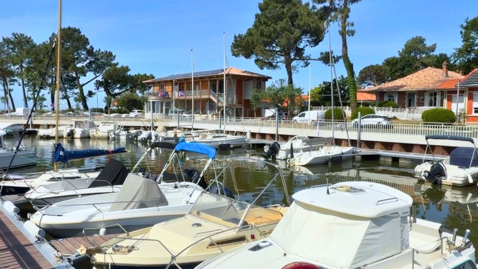 bateaux dans un port, derrière un batiment en bois et de spins. Ciel bleu