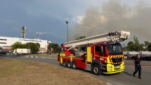 camion de pompier devant une usine d'ou s'échappe de la fumée