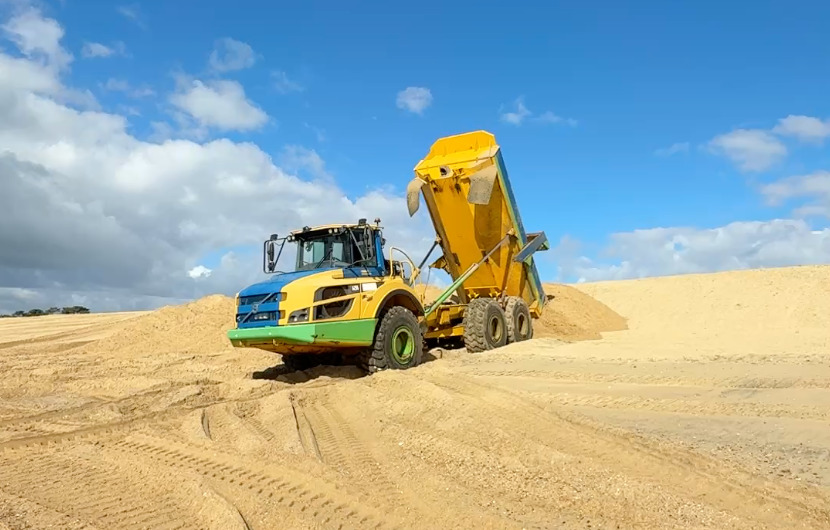 Un camion dépose sa cargaison de sable sur une plage. grand ciel bleu.