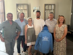 Un groupe de 6 personnes posent dans une salle derrière une vareuse bleue "V-Cabanes en fête"
