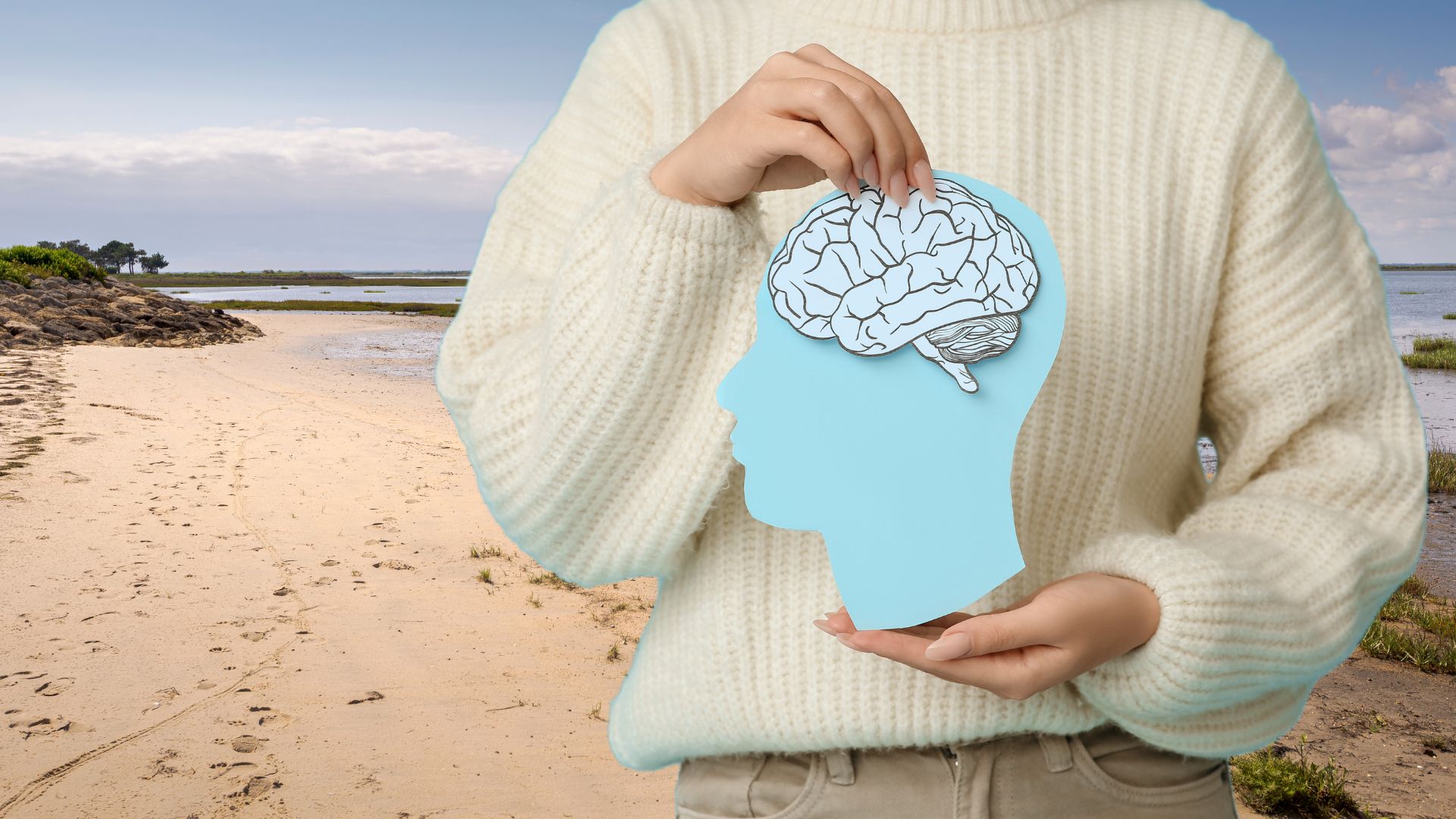 Une personne dans un pull beige tient dans ses mains le schéma d'un cerveau. Derrière unfond avec une plage à marée basse