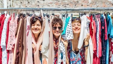 trois femmes passent leur tete dans un rayonnage de vetements