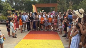 Un groupe de personnes coupe un ruban tricolore davant un passage piéton arc-en-ciel