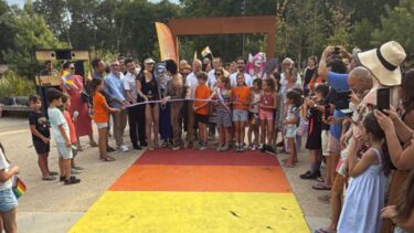 Un groupe de personnes coupe un ruban tricolore davant un passage piéton arc-en-ciel