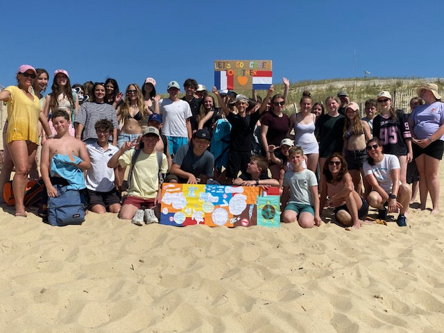 Des collégiens sont en groupe sur la plage et tiennent des pancartes dans leurs mains