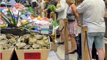 Plusieurs individus attendent en file pour acheter les produits d'un commerçant au sein d'un marché couvert.