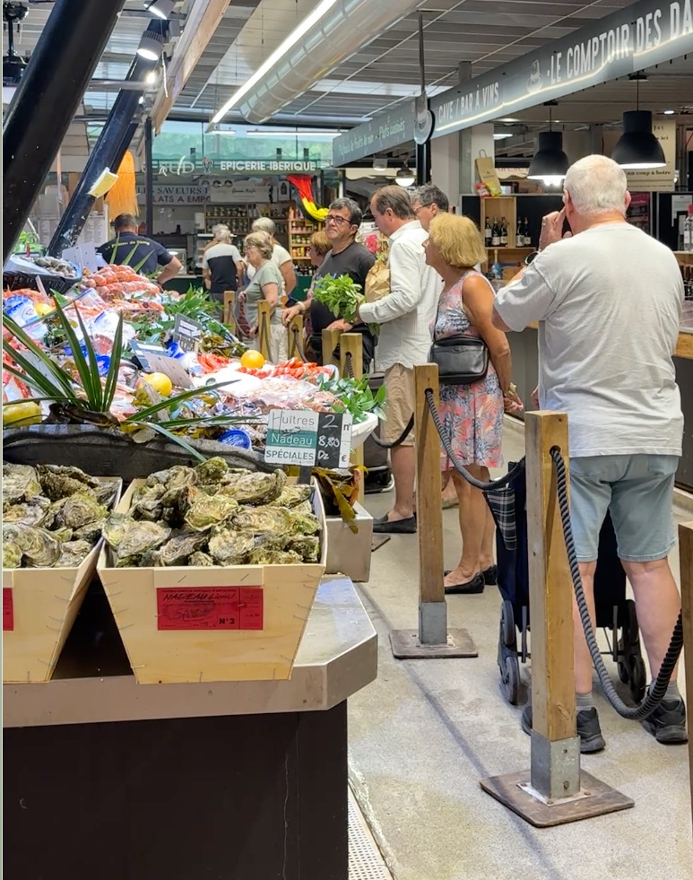 Plusieurs individus attendent en file pour acheter les produits d'un commerçant au sein d'un marché couvert.