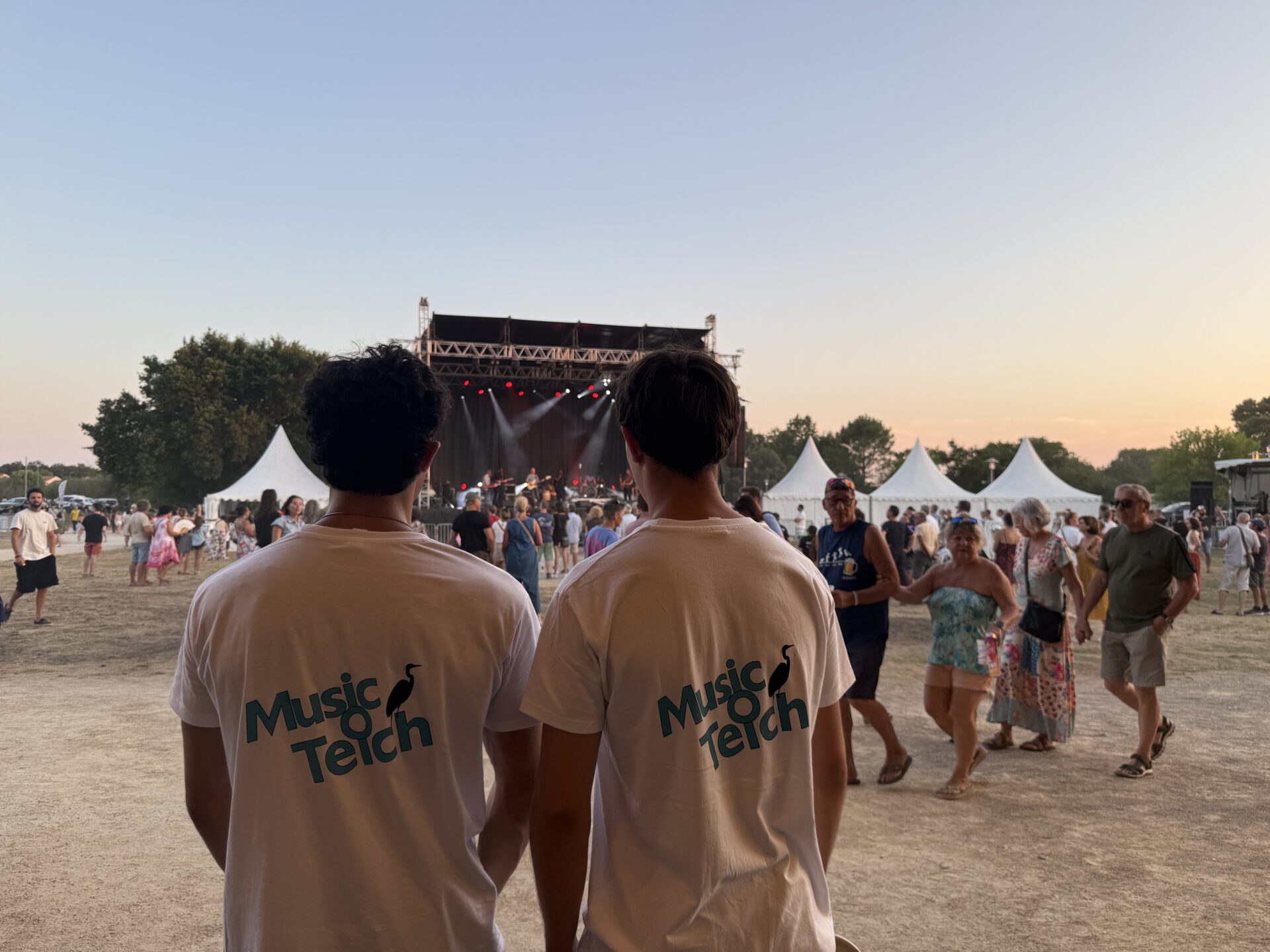 Deux bénévoles font face à la grande scène de Music O Teich. Tous deux portent le tee-shirt du festival, blanc avec un écriture "Music O Teich bleu cyan.
