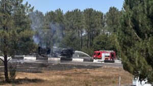 un camion de pompier rouge asperge d'eau un camion transportant du bois en feu sur une route bordée d'arbre