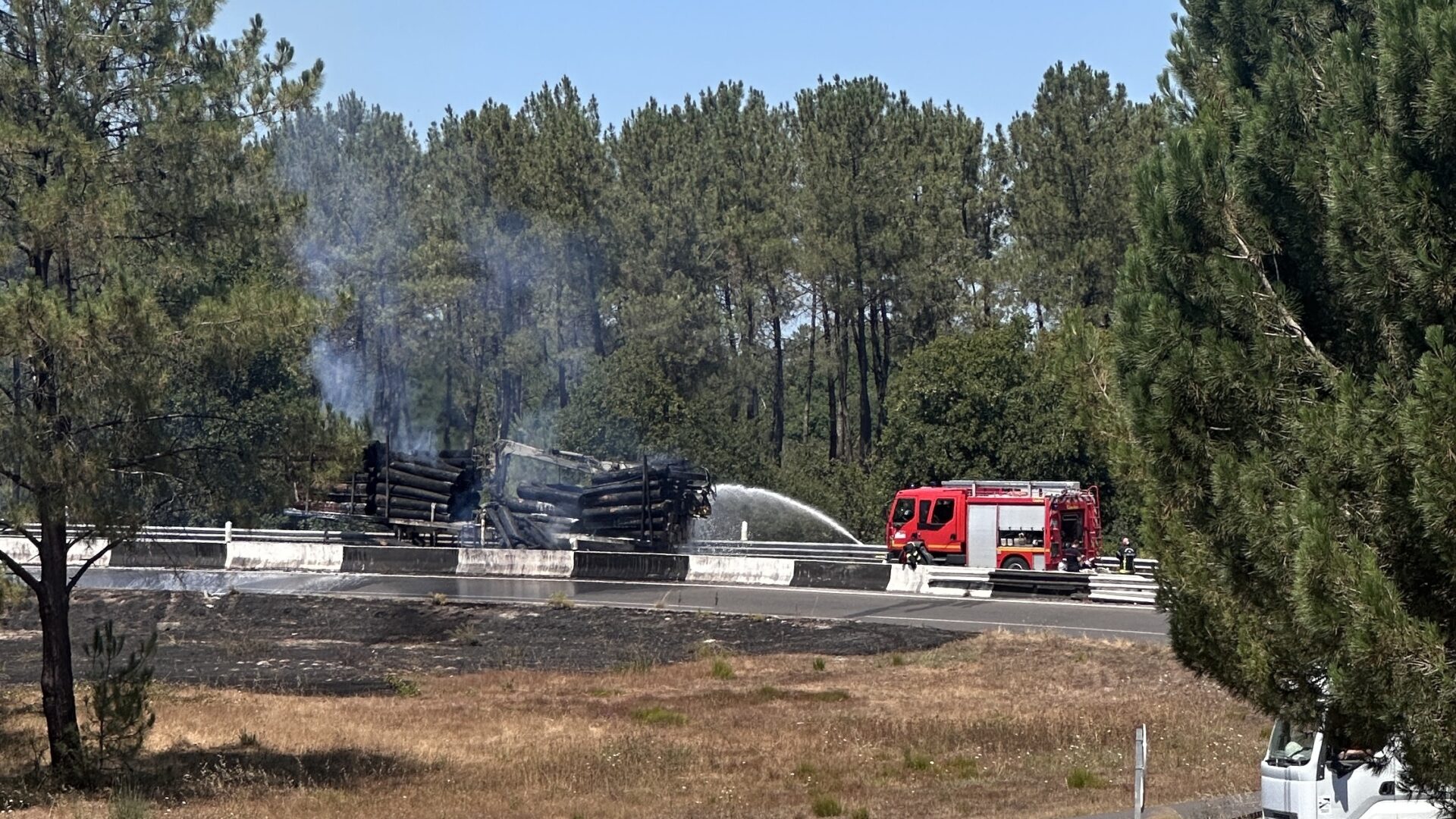 un camion de pompier rouge asperge d'eau un camion transportant du bois en feu sur une route bordée d'arbre