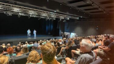 un public dans une salle, deux personnes sur scène