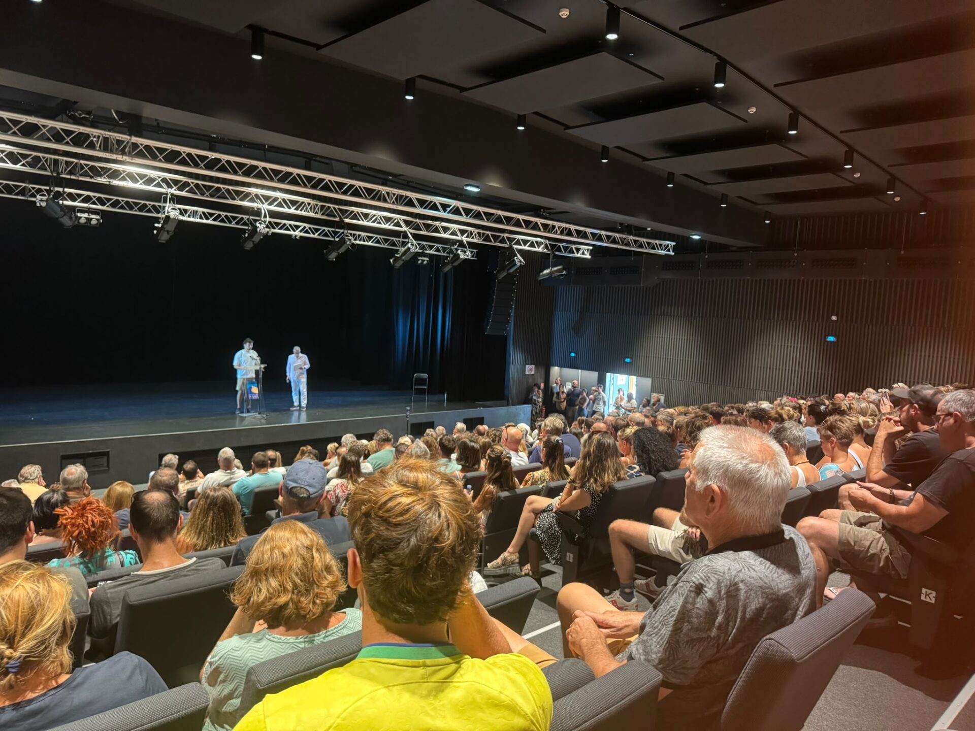 un public dans une salle, deux personnes sur scène