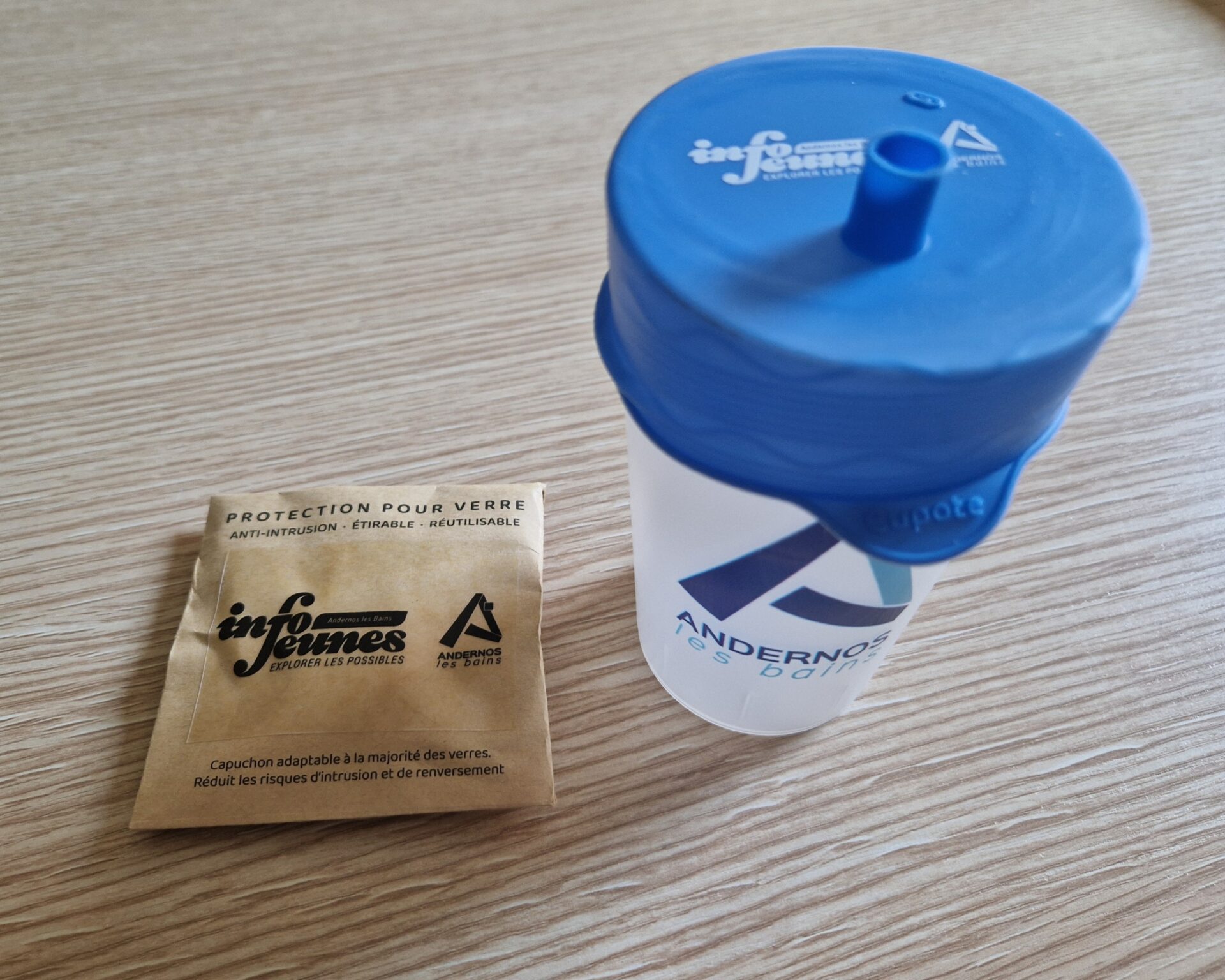 Un verre avec une cupote dessus à droite et à gauche, il y a le sachet où se trouve la cupote.