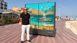 homme avec un polo noir et un pantalon blanc devant une oeuvre artistiques colorée sur le front de mer d'arcachon