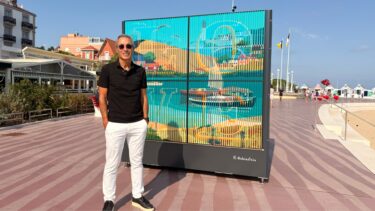 homme avec un polo noir et un pantalon blanc devant une oeuvre artistiques colorée sur le front de mer d'arcachon