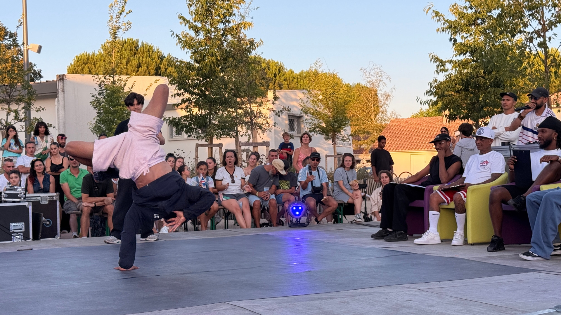 jeune danseur de hip-hop qui réalise une figure sur une scène avec le public en arrière plan et les juges sur la droite