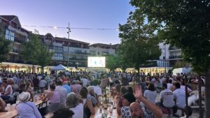 fan zone sur la place du marché de la teste : de nombreuses personnes assises à des tables avec un écran géant en fond