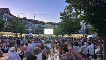 fan zone sur la place du marché de la teste : de nombreuses personnes assises à des tables avec un écran géant en fond