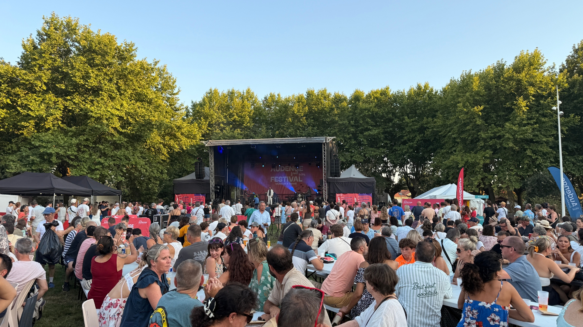 audnege fait son festival : une grande scène avec une foule de personnes devant debout et assises à des tables