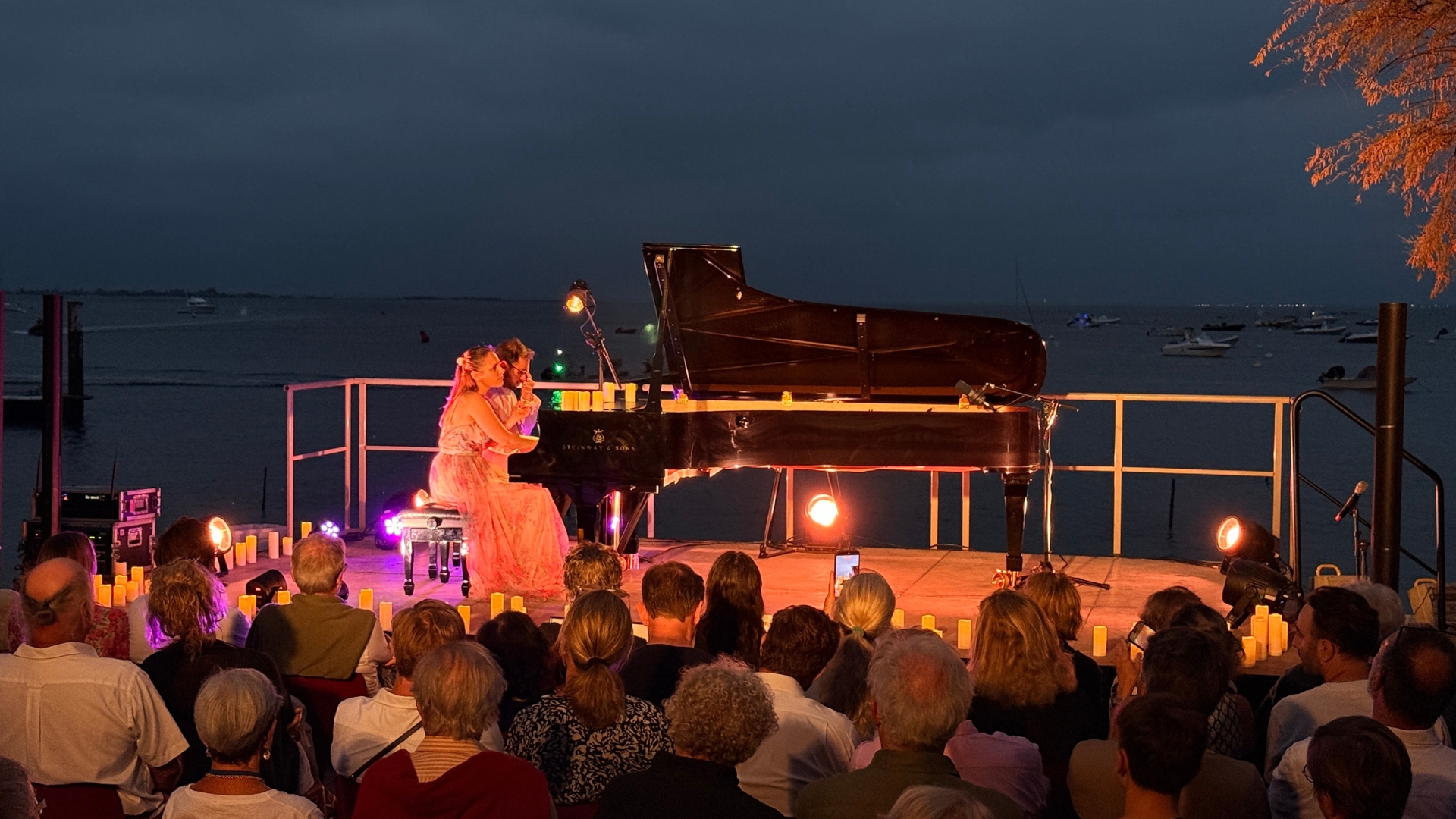 deux pianistes sur la scène du cap ferret music festival avec la mer en arrière plan, de nuit avec des spectateurs au premier plan