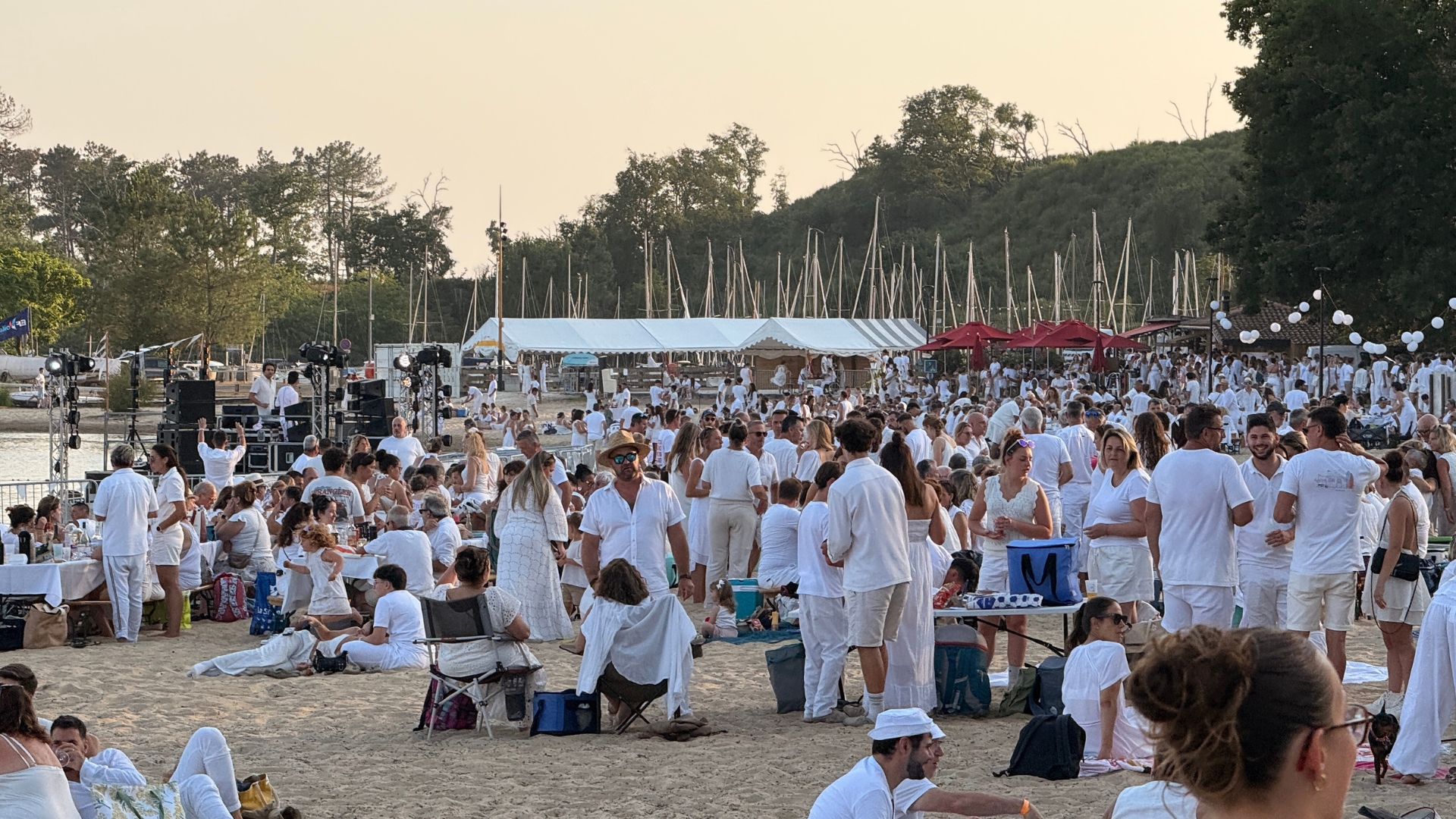 des personnes assises dans le sable et à table, toutes en blanc pour la soirée blanche de cazeaux