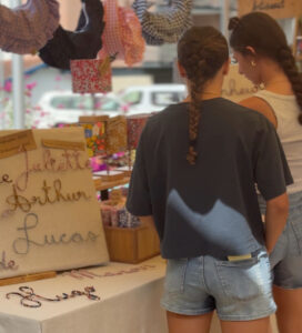 Deux jeunes femmes observent les créations colorées et en tissus d'une artisane.
