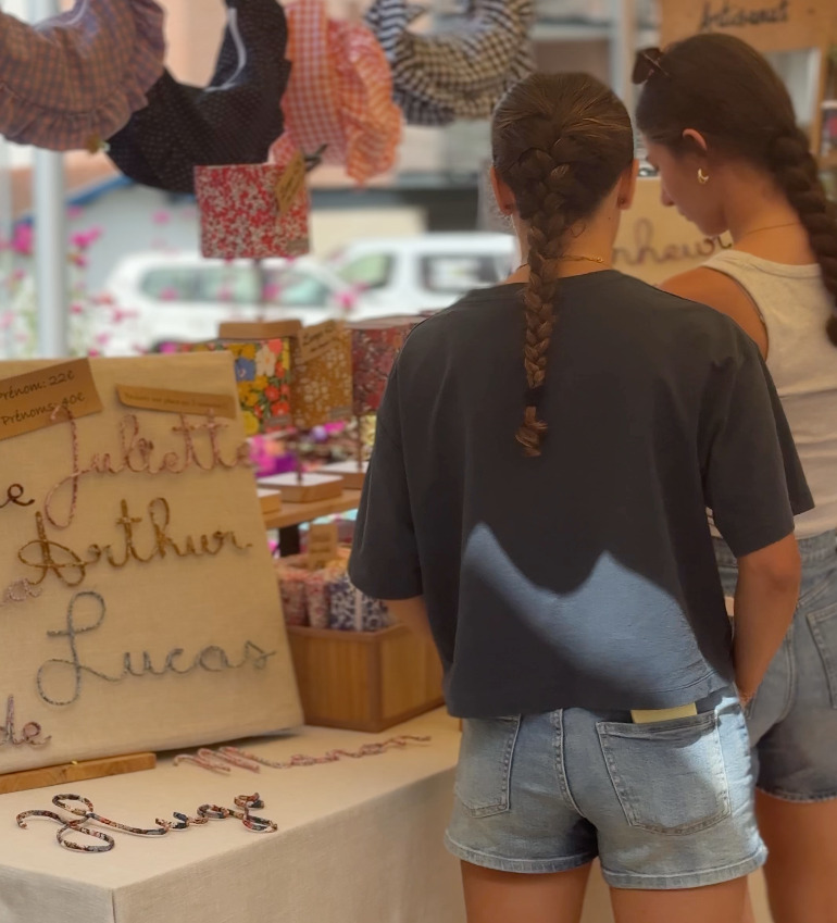 Deux jeunes femmes observent les créations colorées et en tissus d'une artisane.