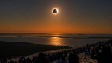 eclipse solaire qui se reflete sur l'eau depuis une dune de sable