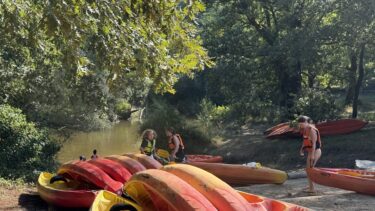 Plusieurs canoë rouge et jaune sont sur une plage près de la Leyre