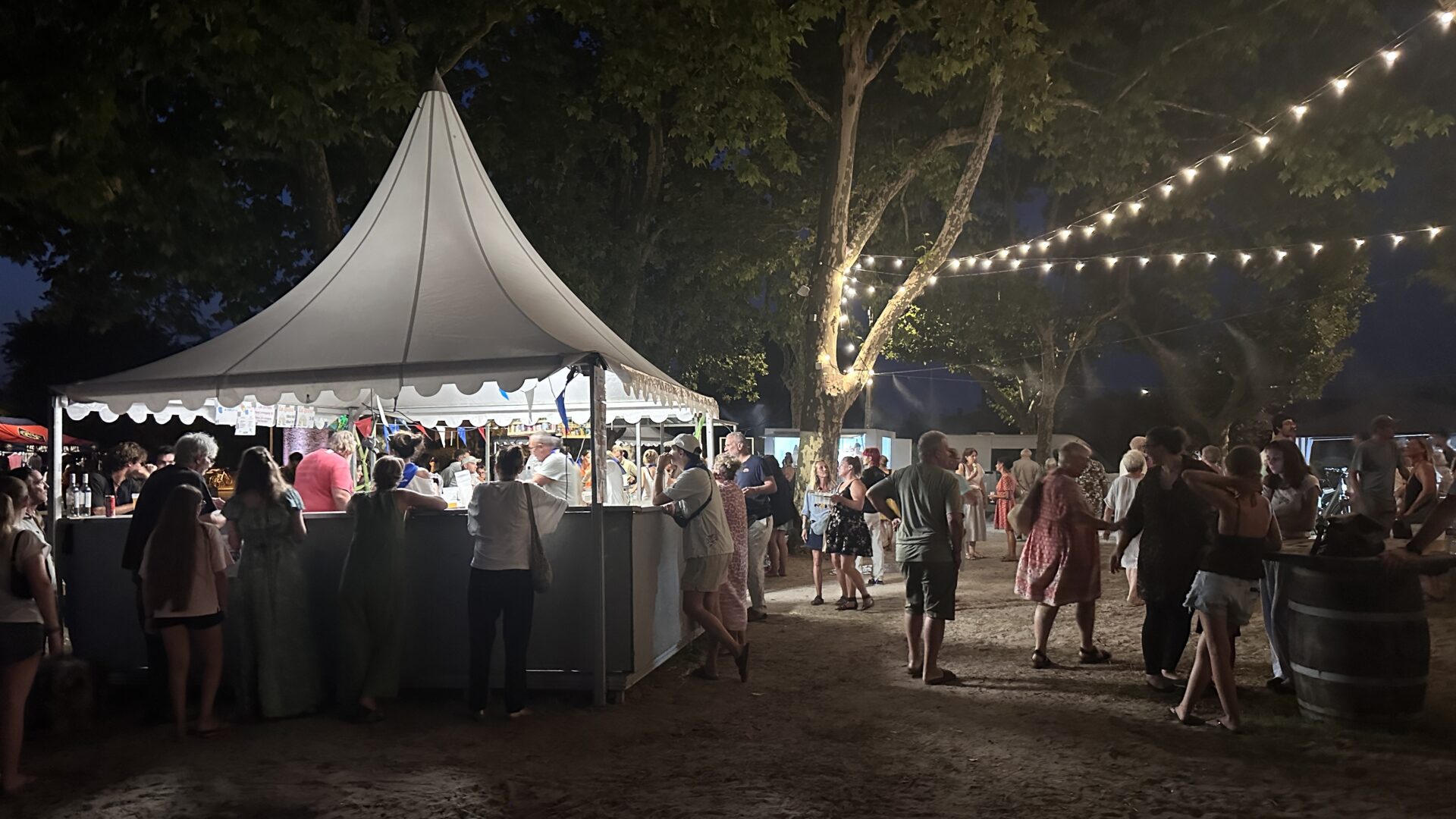 Le marché gourmand d'Arès de nuit. On peut voir, une tente et une foule devant celle-ci.