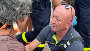 Un secouriste est agenouillé auprès d'une victime afin de dresser une premier diagnostic, entouré par ses équipes et des passants.