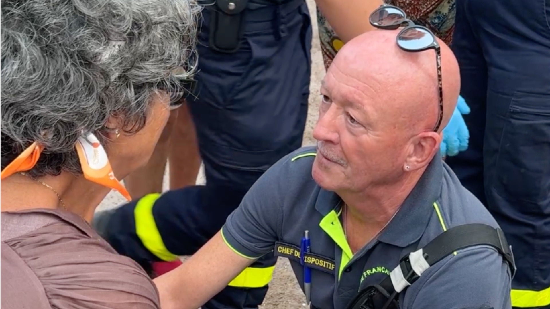 Un secouriste est agenouillé auprès d'une victime afin de dresser une premier diagnostic, entouré par ses équipes et des passants.