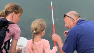 Une jeune fille tient une canne à pêche tandis qu'un animateur lui parle sur sa gauche.