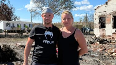 Un homme et une femme se tiennent cote à cote devant une maison brulée, derrière il y a un mobilhome