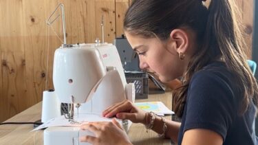 Une jeune fille devant sa machine à coudre pratique un exercice de couture pour apprendre à manier sa machine.