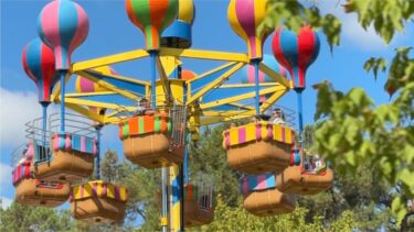 un manege avec des mini montgolfière dans les airs derrière une arbre