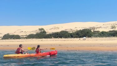 deux personnes dans un canoe rouge et jaune devant une dune de sable