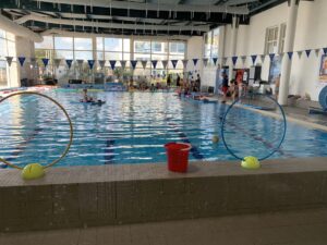 des enfants dans une piscine publique, des fanions au plafond, une nerrière en fond