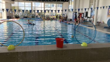 des enfants dans une piscine publique, des fanions au plafond, une nerrière en fond
