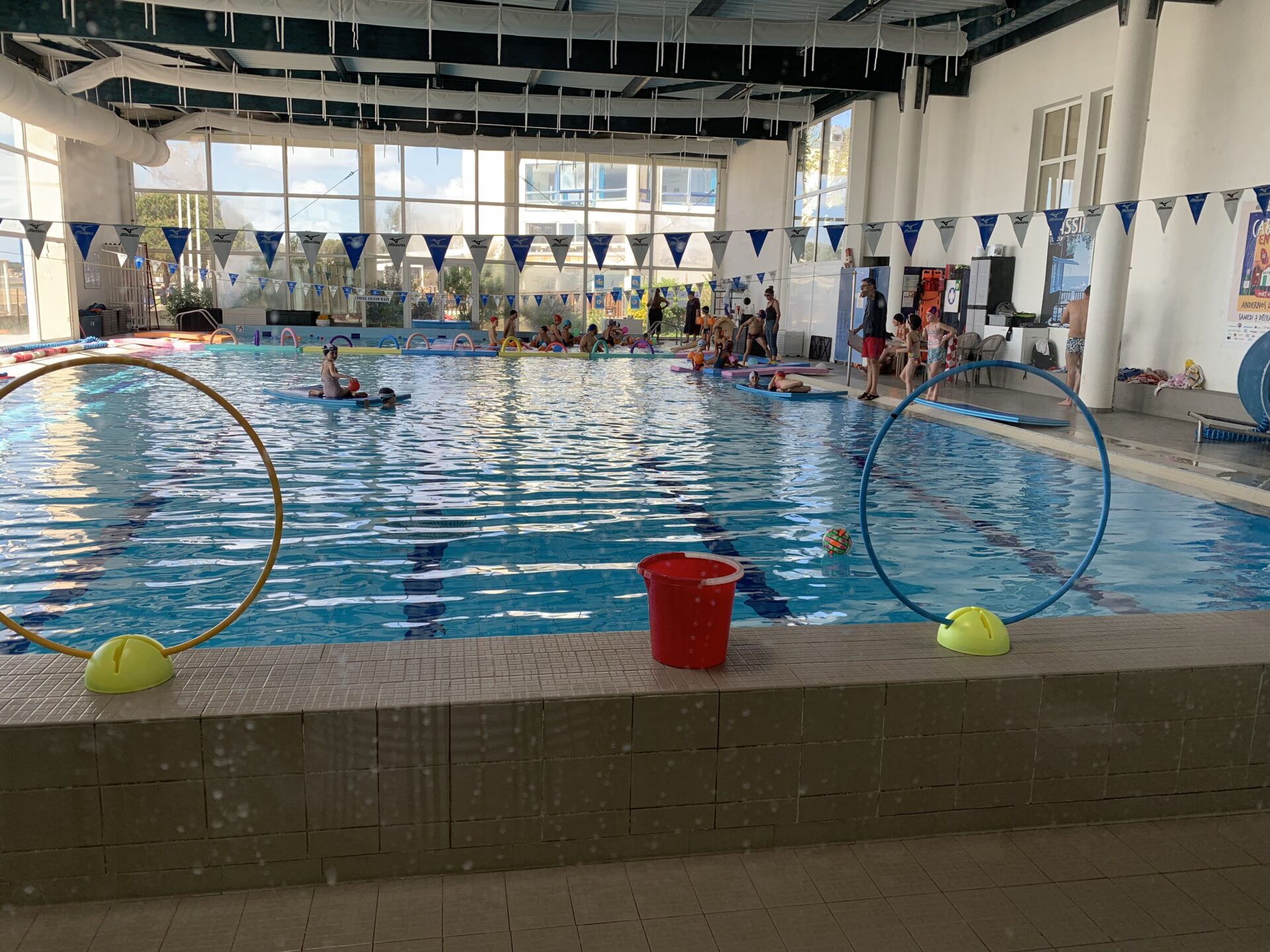 des enfants dans une piscine publique, des fanions au plafond, une nerrière en fond